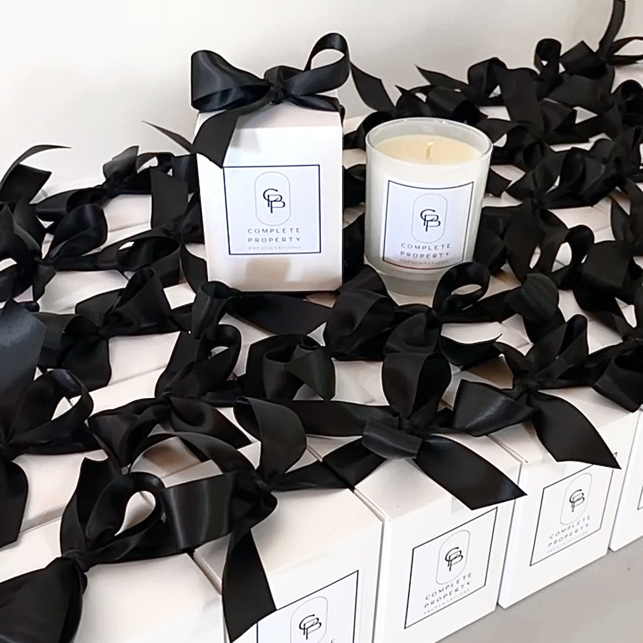 Custom branded 200g soy candles for Complete Property Presentations. Luxe white boxes with black ribbon and logo labels, ideal for real estate gifting.