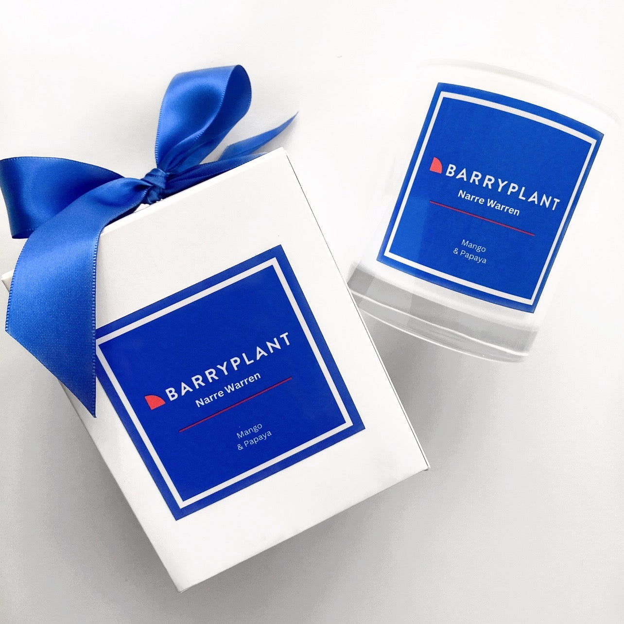 Custom Branded Candle for Barry Plant Narre Warren featuring a Mango & Papaya scent in a 300g white jar with royal blue ribbon and logo label.