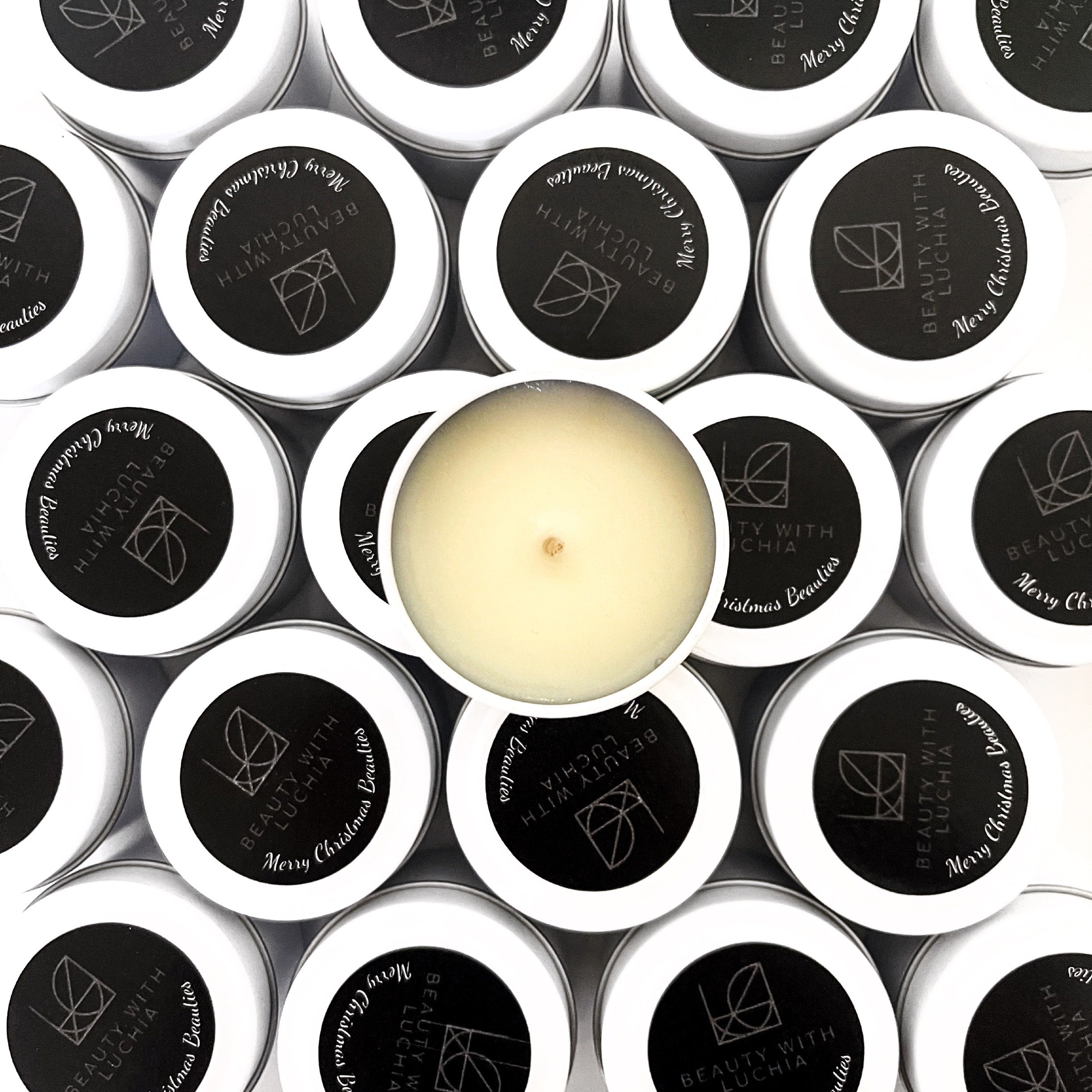 Custom-Branded white tin candles for Beauty With Luchia featuring sleek black lids and a centered soy candle with the lid off.