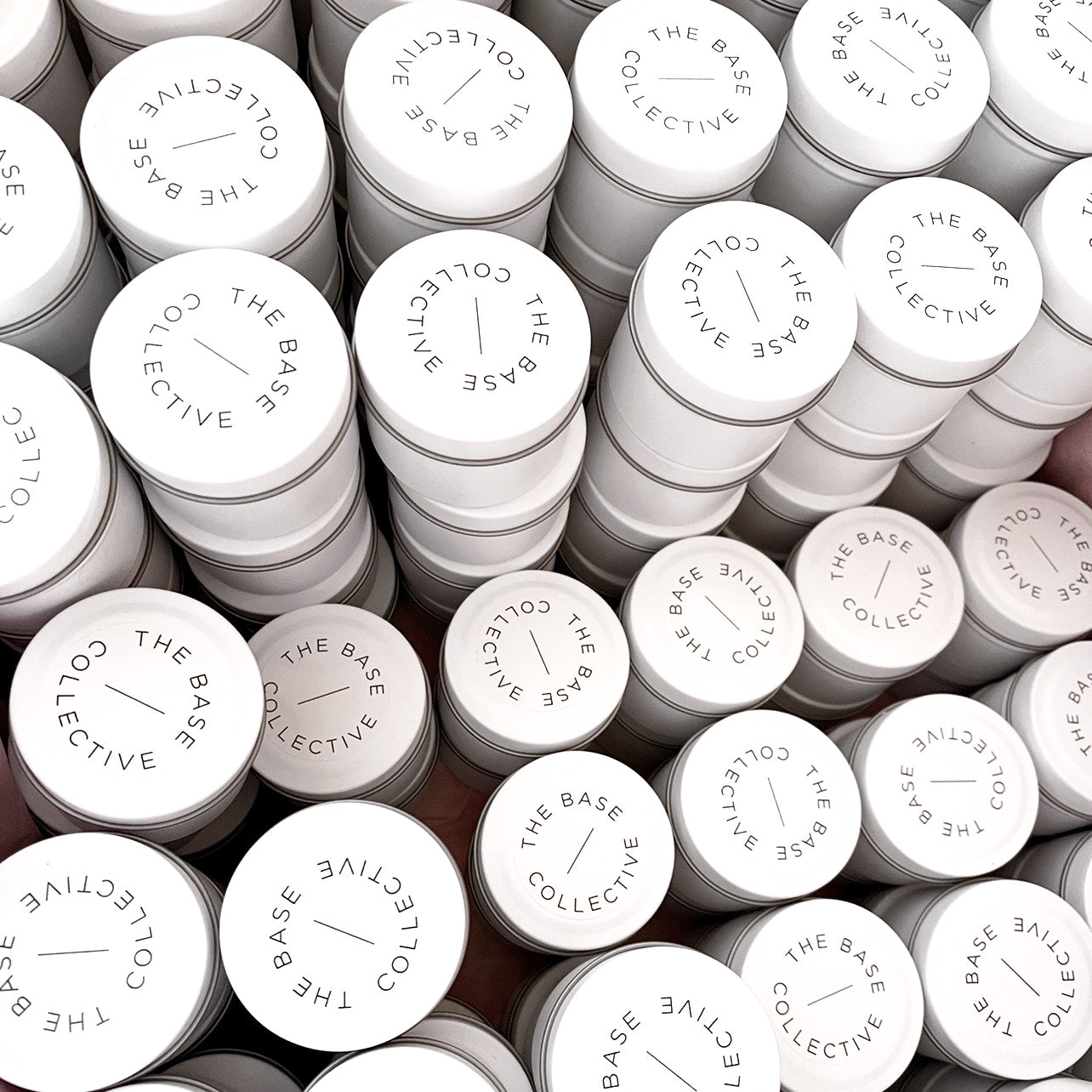 Flatlay of white Custom-Branded tin candles with minimalist labels for The Base Collective, stacked and arranged in a grid.