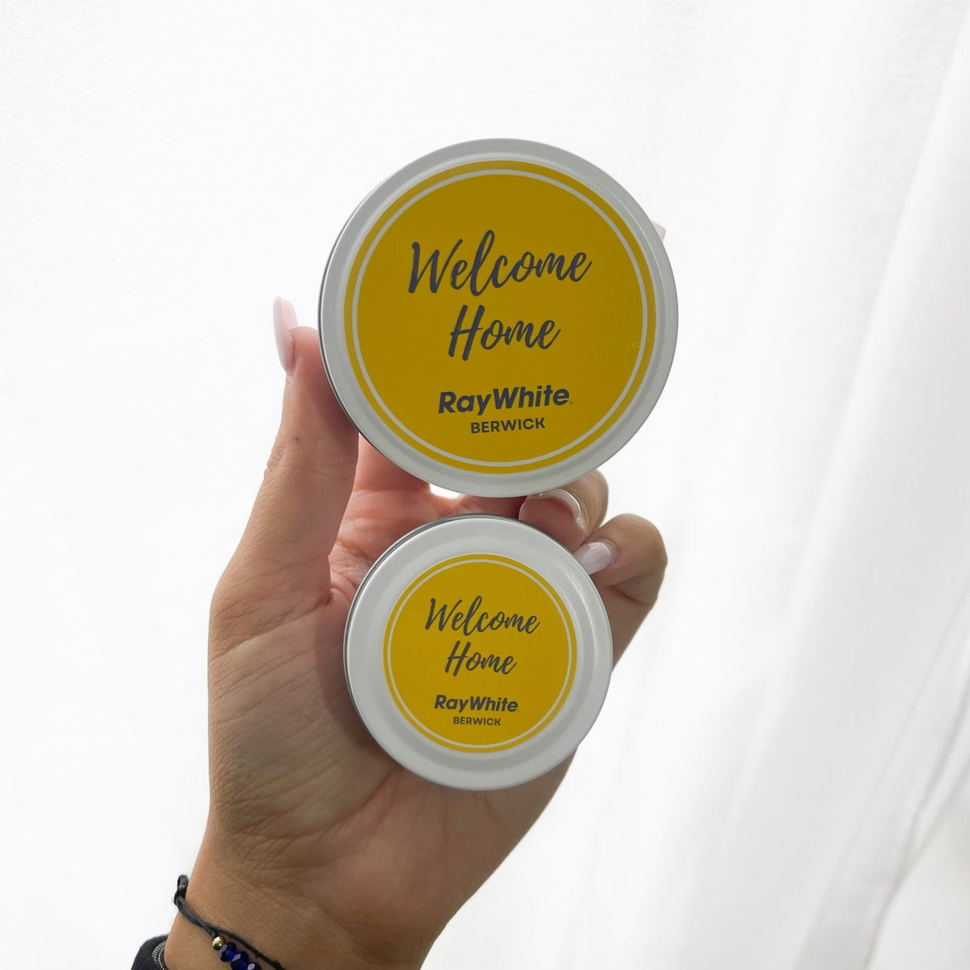 White tin candles with bright yellow ‘Welcome Home’ labels for Ray White Berwick, styled for real estate gifting.