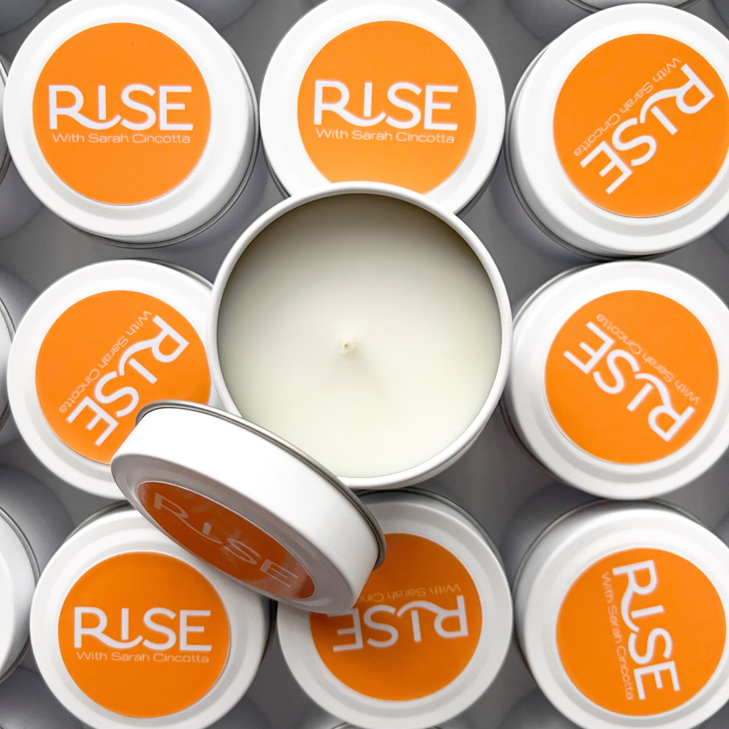 Branded candle tins for Rise with Sarah Cincotta, featuring a bold orange label design on clean white tins.