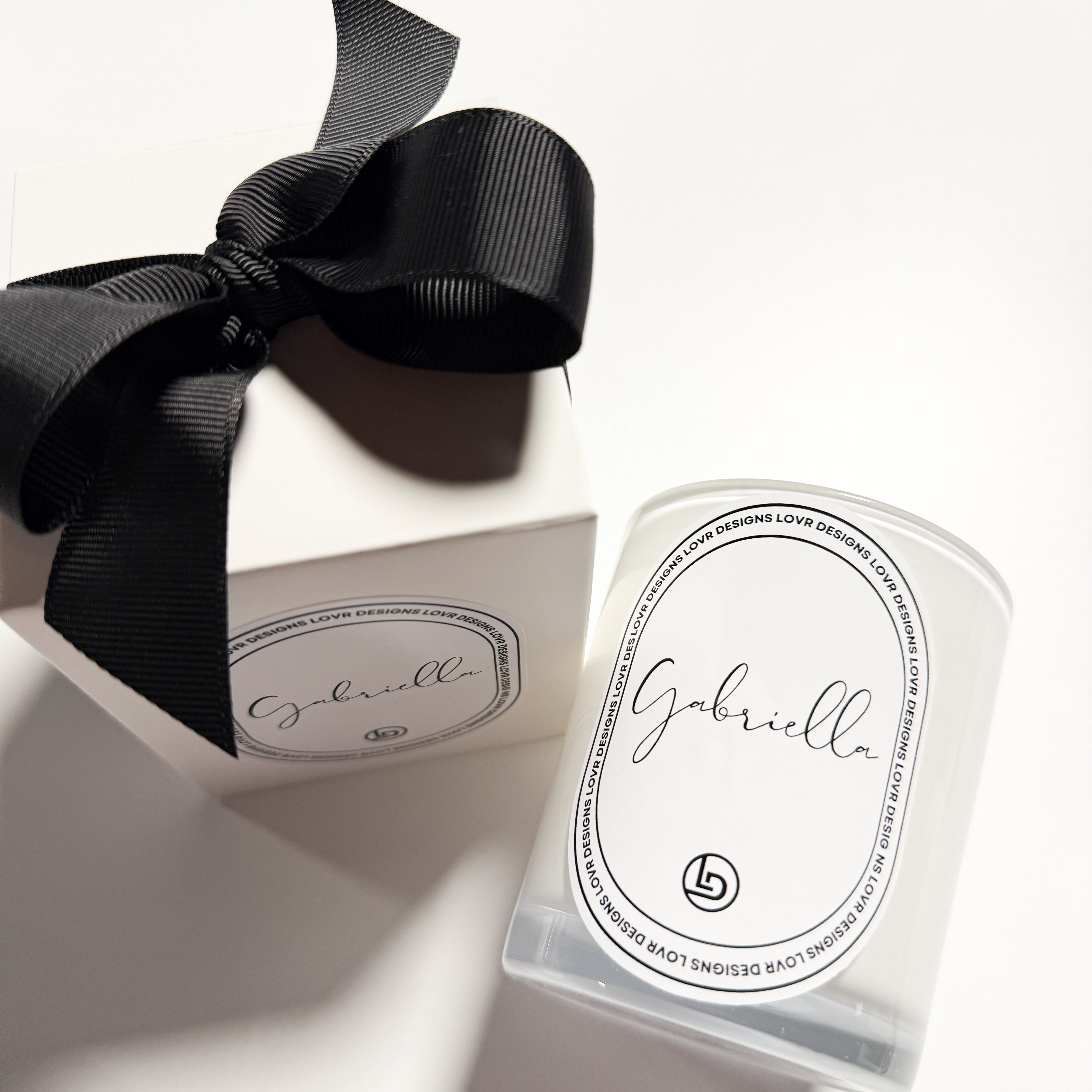 Lovr Designs personalised ‘Gabriella’ scented soy candle jar next to its luxe white gift box wrapped in a black ribbon. Handcrafted in Melbourne with premium soy wax and lead-free cotton wick for up to 35 hours of burn time.