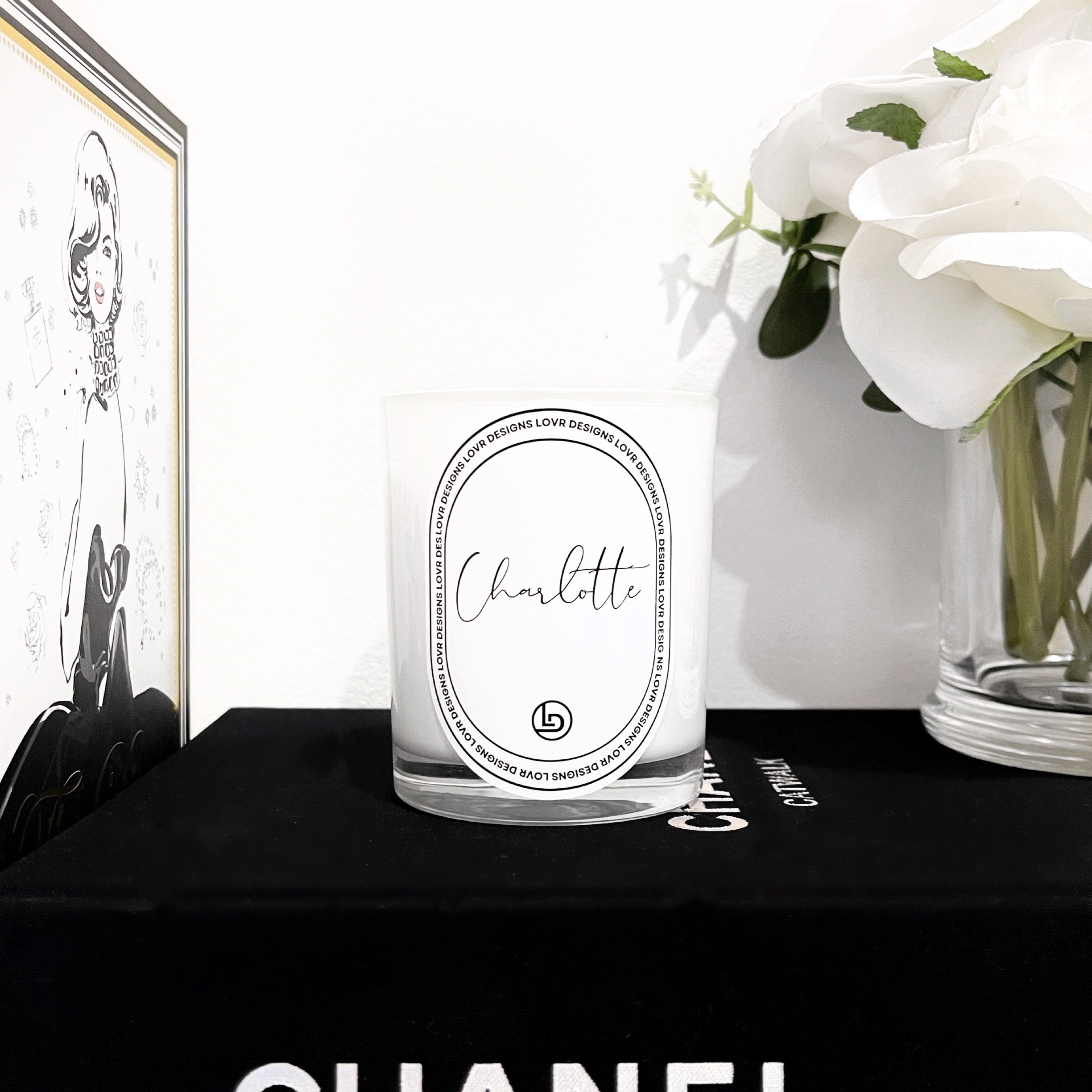 Lovr Designs personalised ‘Charlotte’ Name scented soy candle jar styled atop a black Chanel book with white flowers in the background. Hand-poured in Melbourne and elegantly boxed, this custom name candle makes a chic home décor accent or gift