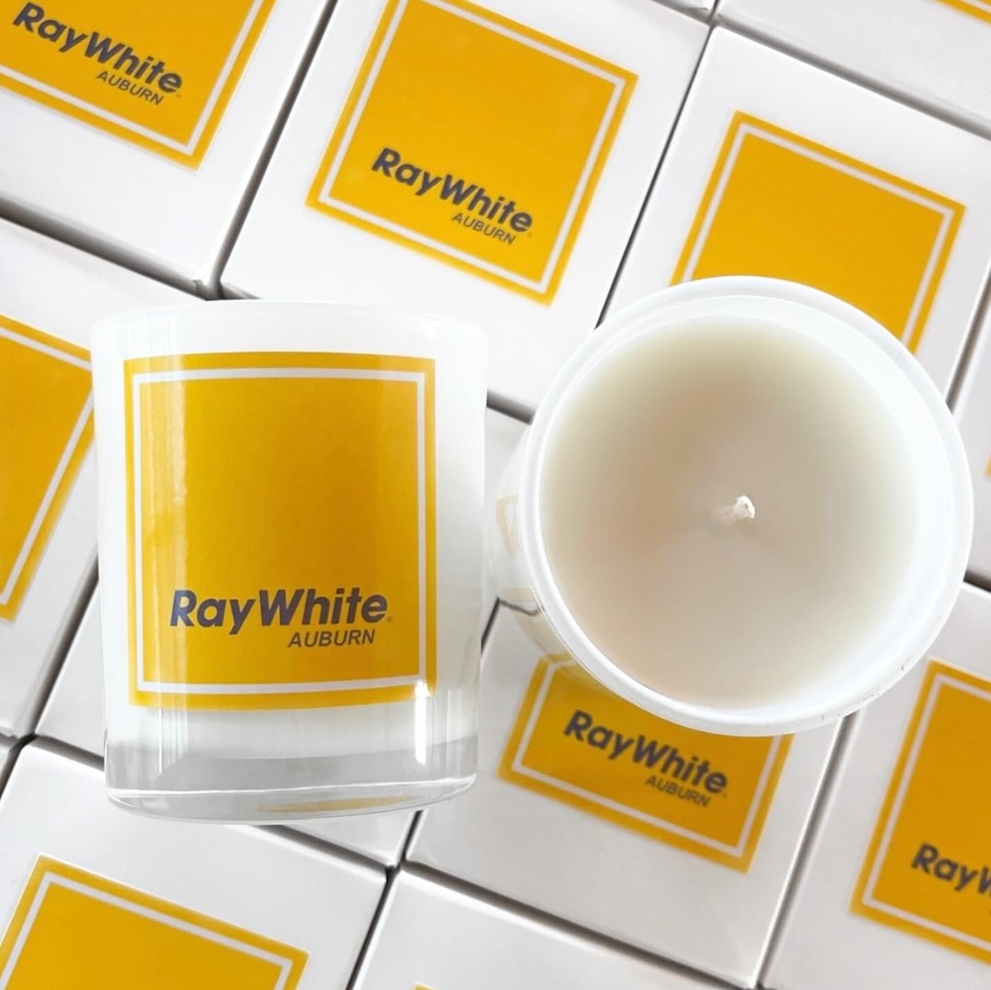 Custom branded 200g soy candles for Ray White Auburn. Bright yellow logo labels on white boxes and jars, ideal for real estate settlement gifts.
