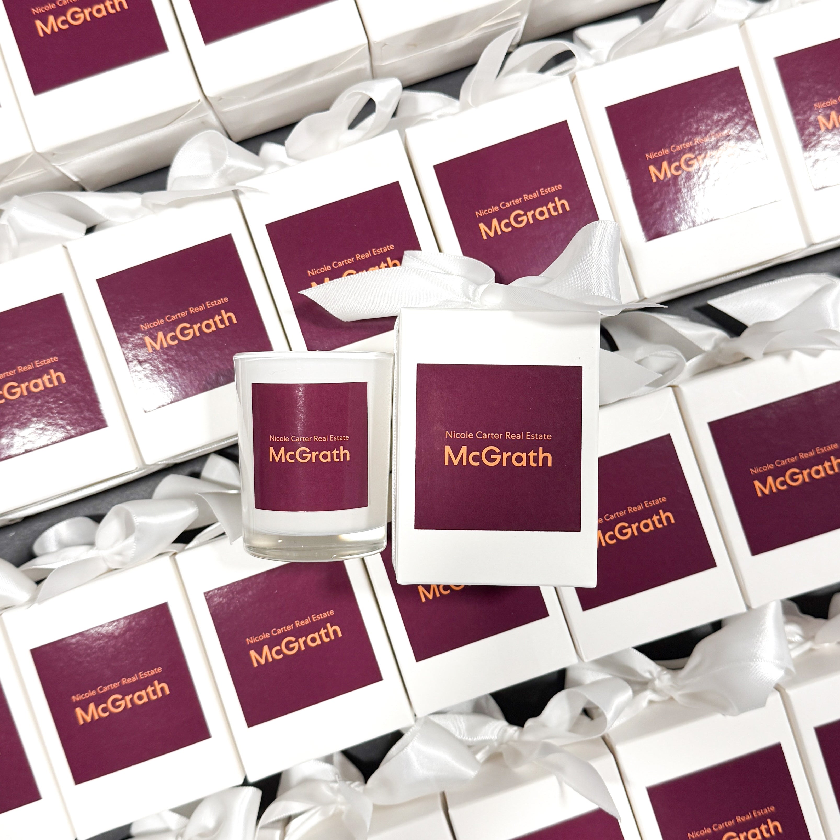 60g custom branded candle with logo for McGrath Real Estate. Pictured in a styled flatlay with white ribbon packaging.