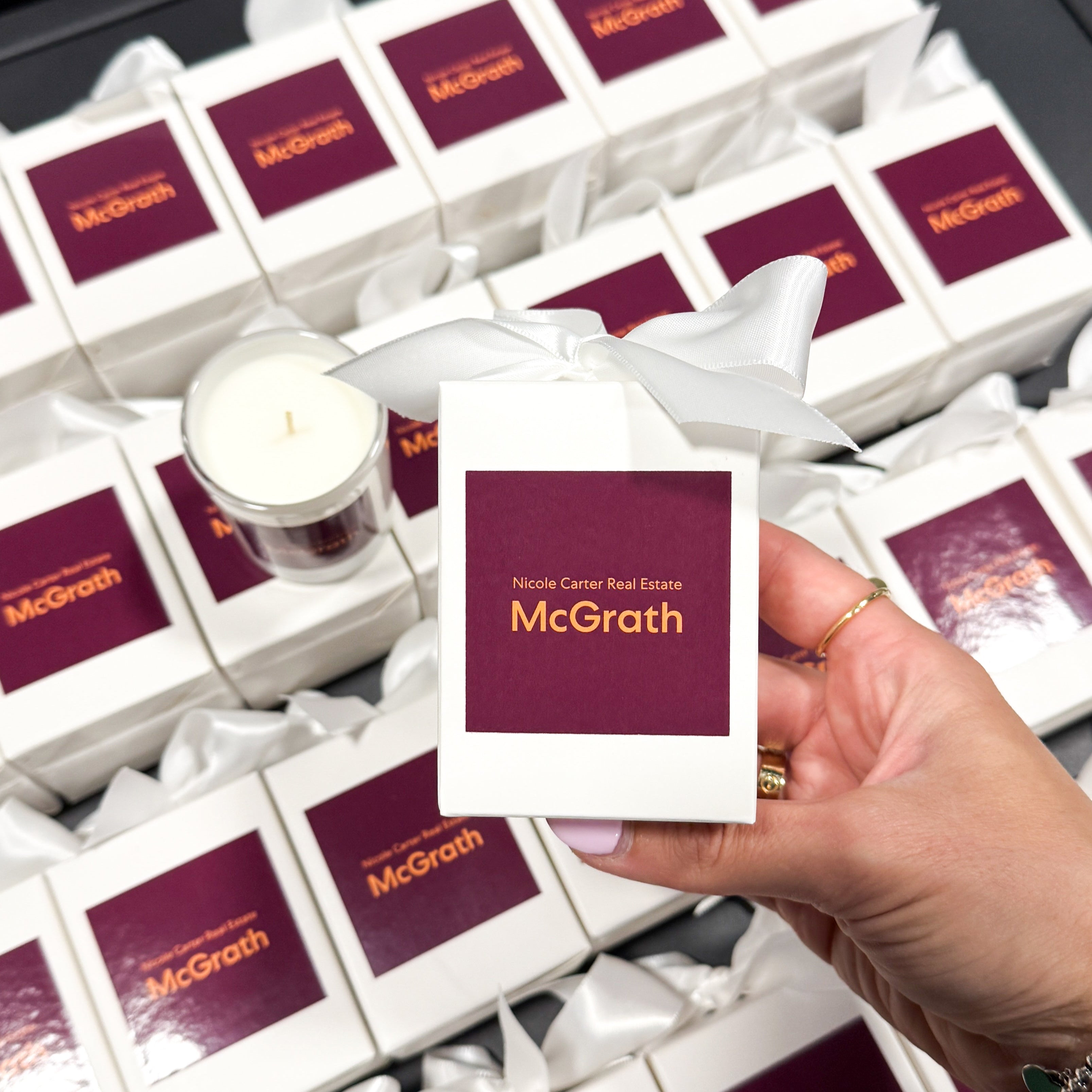 60g custom branded candle with logo for McGrath Real Estate. Pictured in a styled flatlay with white ribbon packaging.