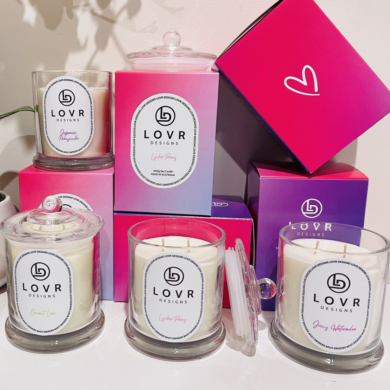 Group display of Lovr Designs Signature Collection candles including Coconut Lime, Lychee Peony, Juicy Watermelon, and Japanese Honeysuckle.