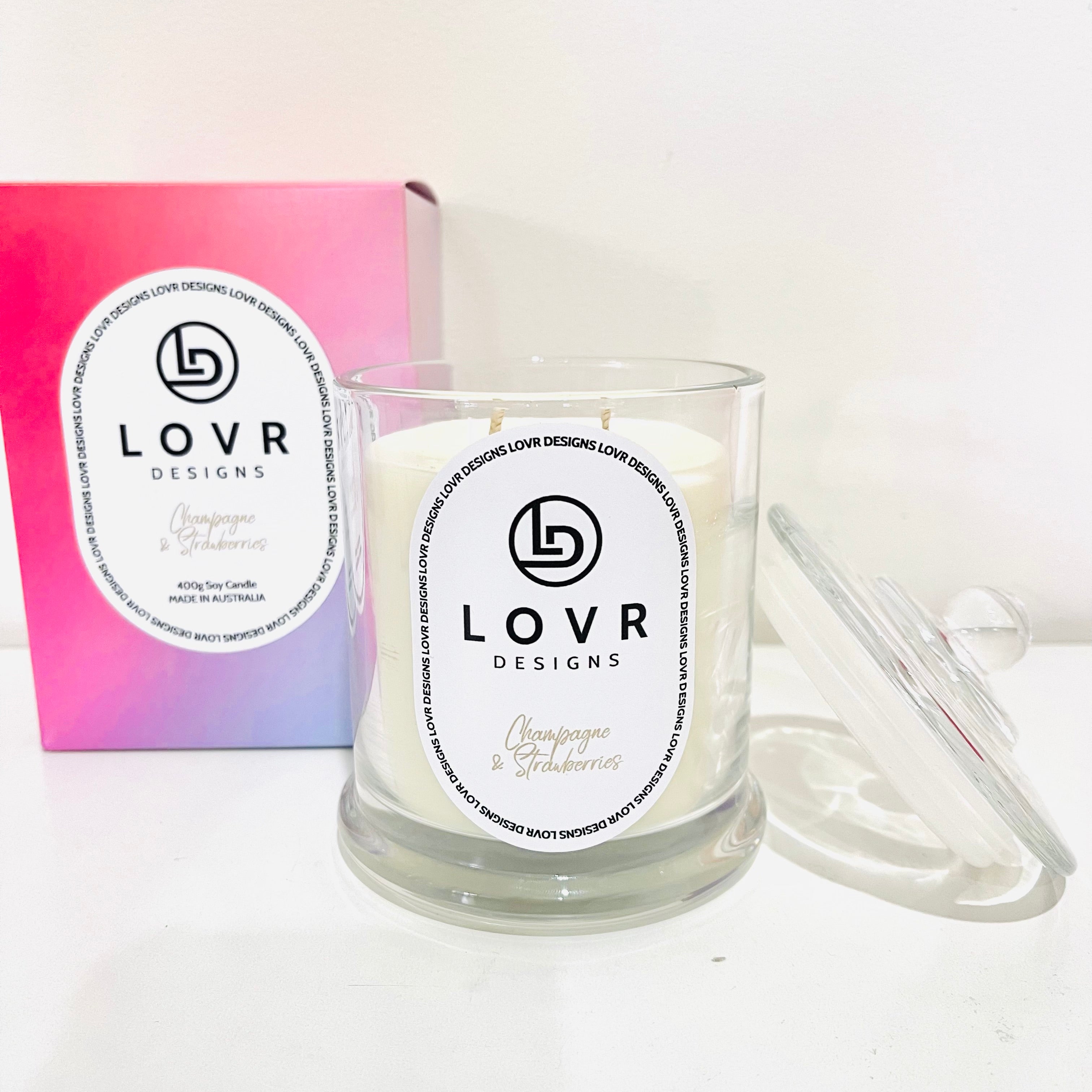 Champagne & Strawberries scented soy candle in clear glass jar with lid, styled beside its pink and purple ombré box – Lovr Designs