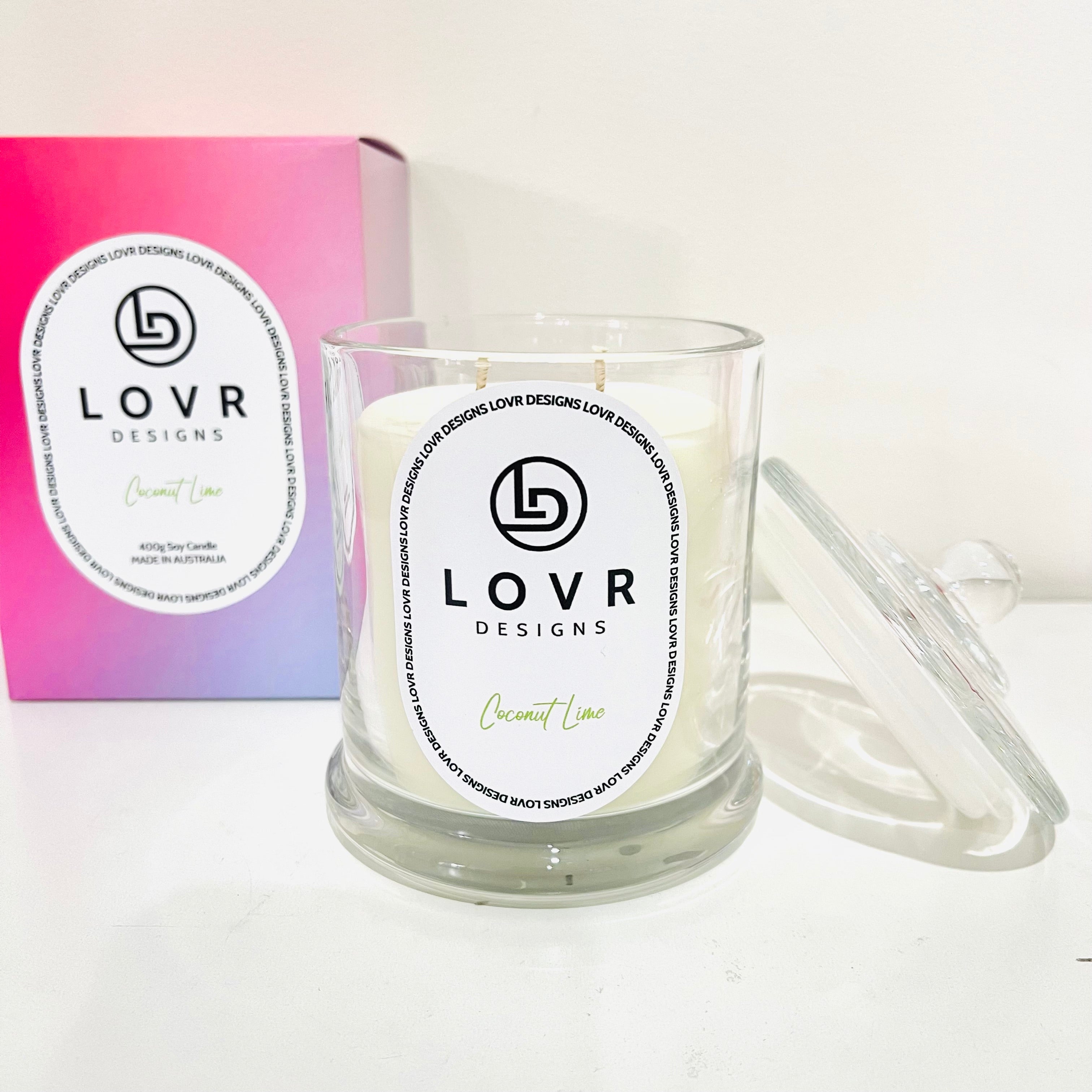 Lovr Designs Coconut Lime 400g scented soy candle in glass jar with lid, shown alongside its ombré pink and purple packaging.