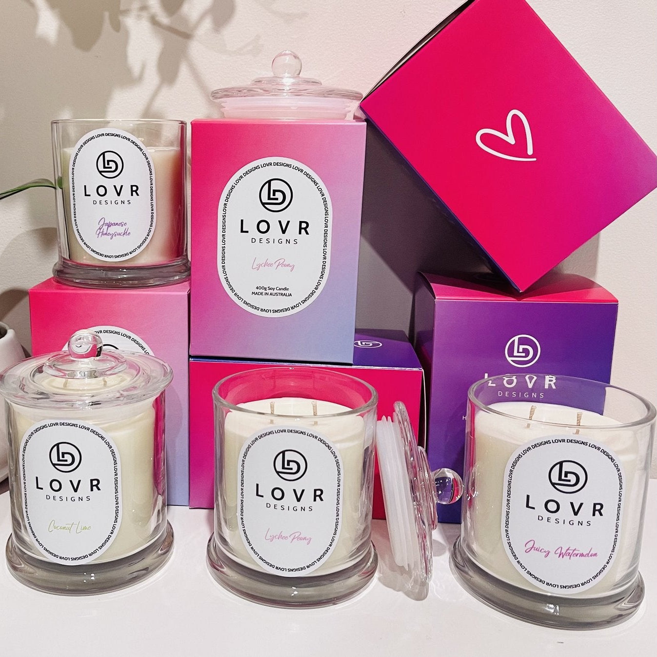 Group display of Lovr Designs Signature Collection candles including Coconut Lime, Lychee Peony, Juicy Watermelon, and Japanese Honeysuckle.