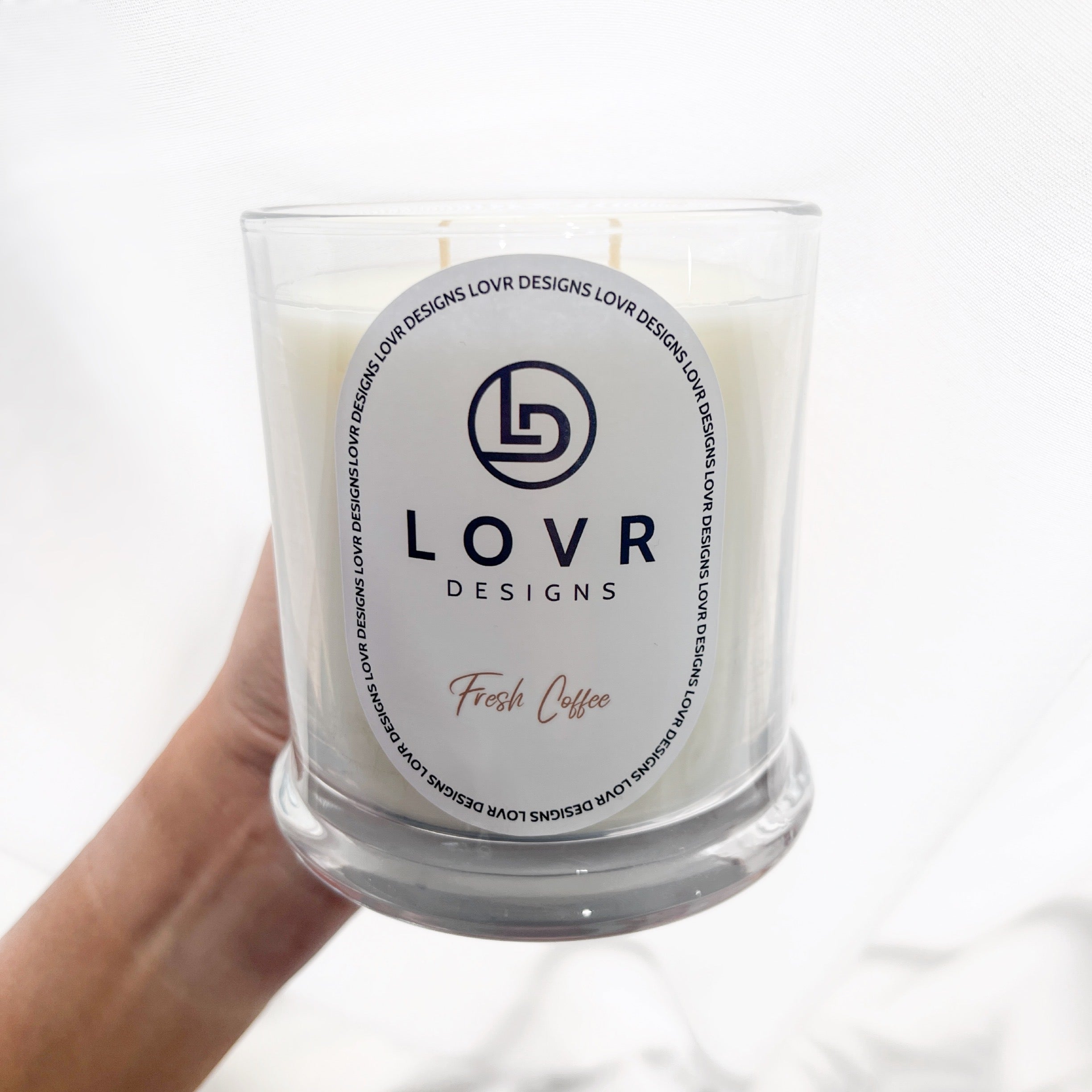Hand holding a Fresh Coffee scented soy candle by Lovr Designs in a clear glass jar with minimalist label.